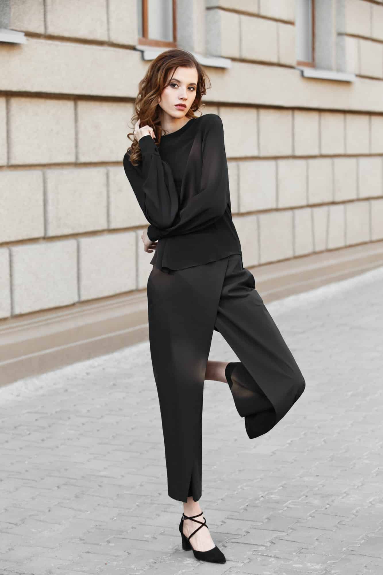 Brunette girl dressed in black blouse and trousers poses in the city street on a sunny day